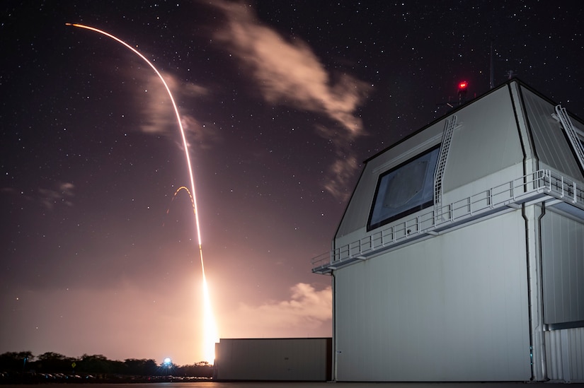 A long-exposure photograph of a night launch of a missile, which leaves a trail of light.