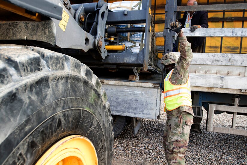 Spc. Desmond Smith, movement specialist, 941st Movement Control Team, works with a white truck driver to guide a forklift in loading a pallet of water at the Syrian Logistics Cell operations center, Erbil, Iraq, Dec. 3, 2019. Once loaded and secured in the truck, the water will be delivered to Syria.