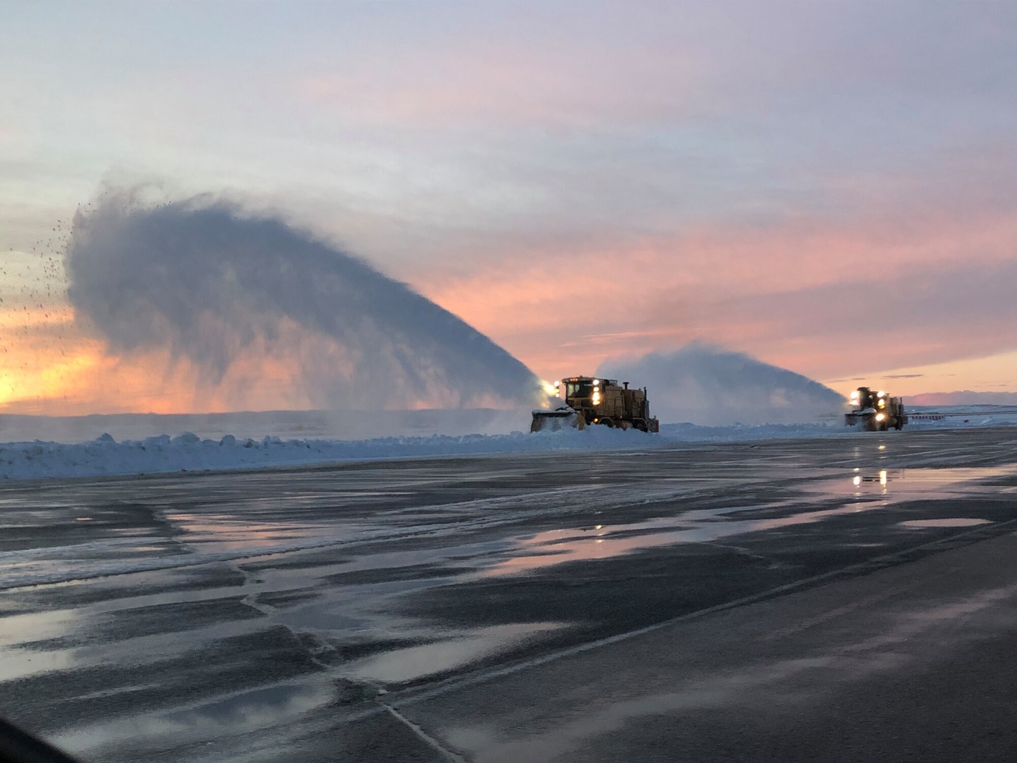 Two snow plows remove snow from a flightline during Sunset at Ellsworth Air Force Base.