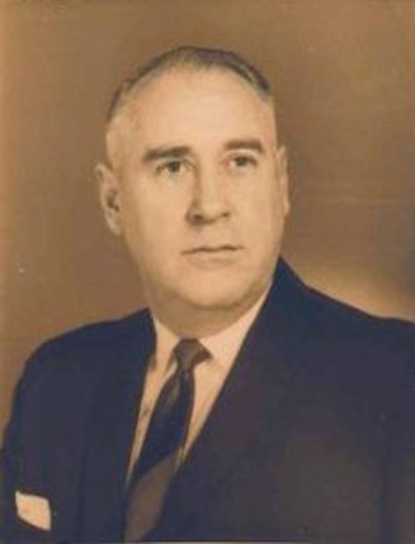 A man in a suit, tie and pocket square poses for an official photo.