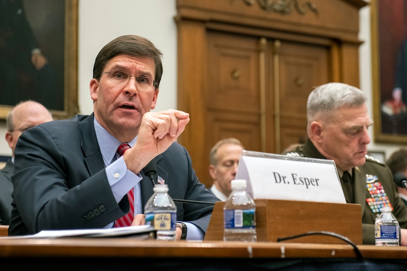 Man in suit gestures while speaking during a congressional hearing.