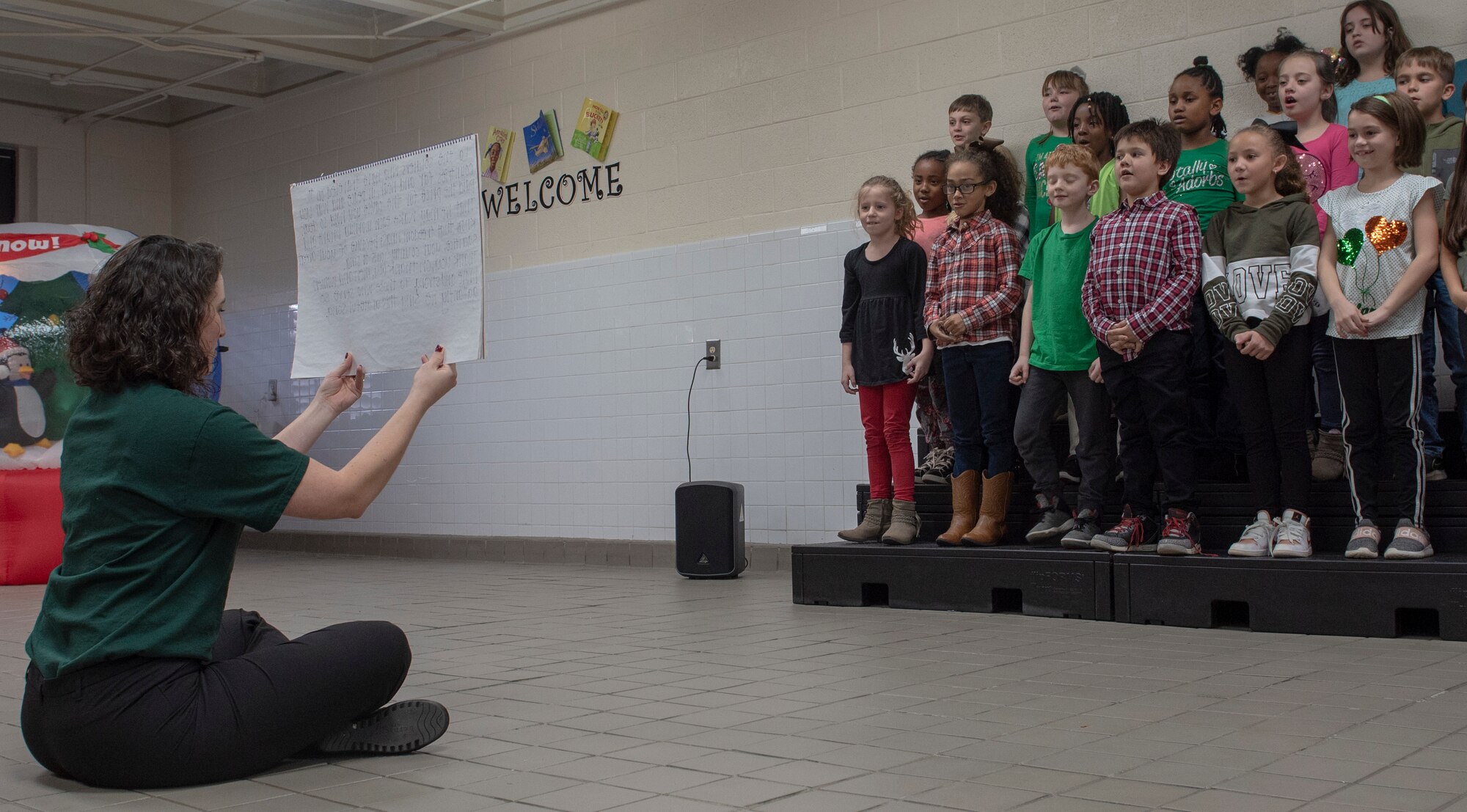 A photo of students watching a teacher hold a notepad.