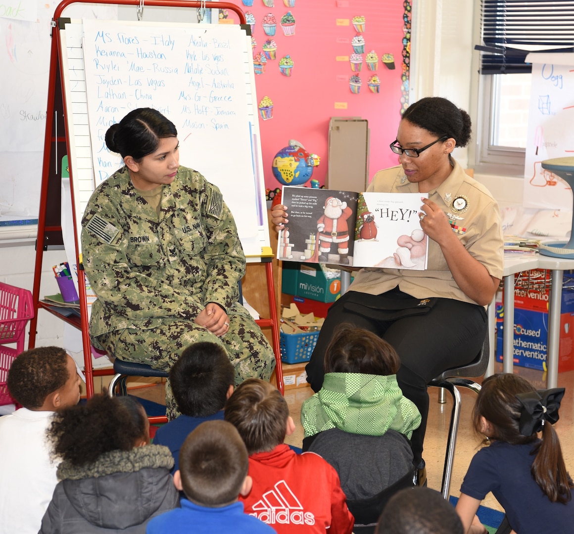 Petty Officer 1st Class Kamitria Delaney (right), assistant command career counselor assigned to Navy Recruiting District San Antonio, joined by Petty Officer 2nd Class Angelica Brown (left), NRD San Antonio’s  community service coordinator, reads to a first-grade class at Dorie Miller Elementary School as part of the school’s annual Pearl Harbor and Dorie Miller Remembrance Program. The event was held in remembrance of those who fought and for those who lost their lives on Dec. 7, 1941.
