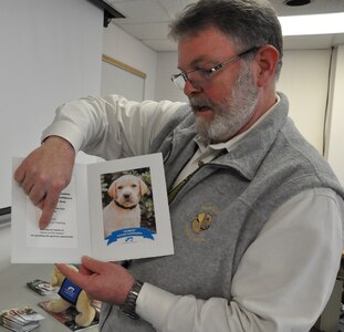 IMAGE: DAHLGREN, Va. (Dec. 11, 2019) – Retired Chief Warrant Officer Ed Hudson shows his photographs of Honor, a dog he named after the Navy core value, and raises through Southeastern Guide Dogs’ tele-raiser program. The Cyber Technologies and Software Systems Division head at Naval Surface Warfare Center Dahlgren Division highlighted his journey with raising guide dogs during a Veterans Integration event, Dec. 5. Hudson has volunteered for Southeastern Guide Dogs, a nonprofit in Florida that provides services to the visually impaired, veterans, children, and teenagers for more than a decade. The Navy veteran who served for 20 years encouraged his fellow veterans to “find something in life that makes you feel like you are not just existing.” (U.S. Navy photo/Released)