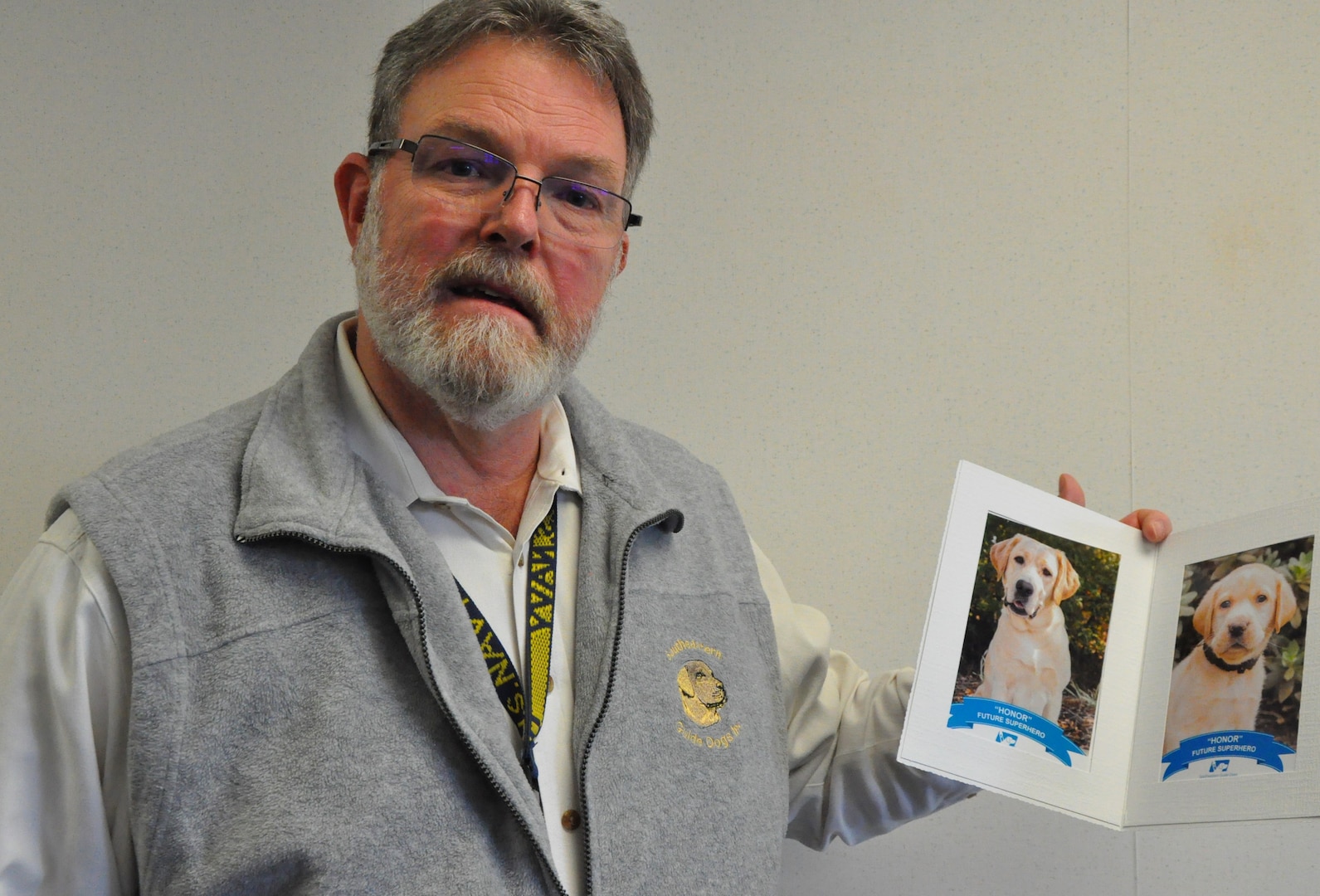 IMAGE: DAHLGREN, Va. (Dec. 11, 2019) – Retired Chief Warrant Officer Ed Hudson shows his photographs of Honor, a dog he named after the Navy core value, and raises through Southeastern Guide Dogs’ tele-raiser program. The Cyber Technologies and Software Systems Division head at Naval Surface Warfare Center Dahlgren Division highlighted his journey with raising guide dogs during a Veterans Integration event, Dec. 5. Hudson has volunteered for Southeastern Guide Dogs, a nonprofit in Florida that provides services to the visually impaired, veterans, children, and teenagers for more than a decade. The Navy veteran who served for 20 years encouraged his fellow veterans to “find something in life that makes you feel like you are not just existing.” (U.S. Navy photo/Released)