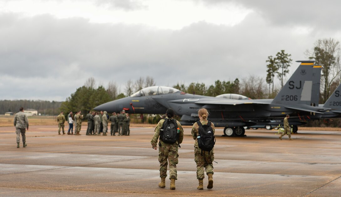 Two Airmen walk toward a group being briefed on the capabilities of the F-15E Strike Eagle Dec. 10, 2019, at Columbus Air Force Base, Miss. An array of avionics and electronics systems gives the F-15E the capability to fight at low altitude, day or night and in all weather. (U.S. Air Force photo by Airman Davis Donaldson)