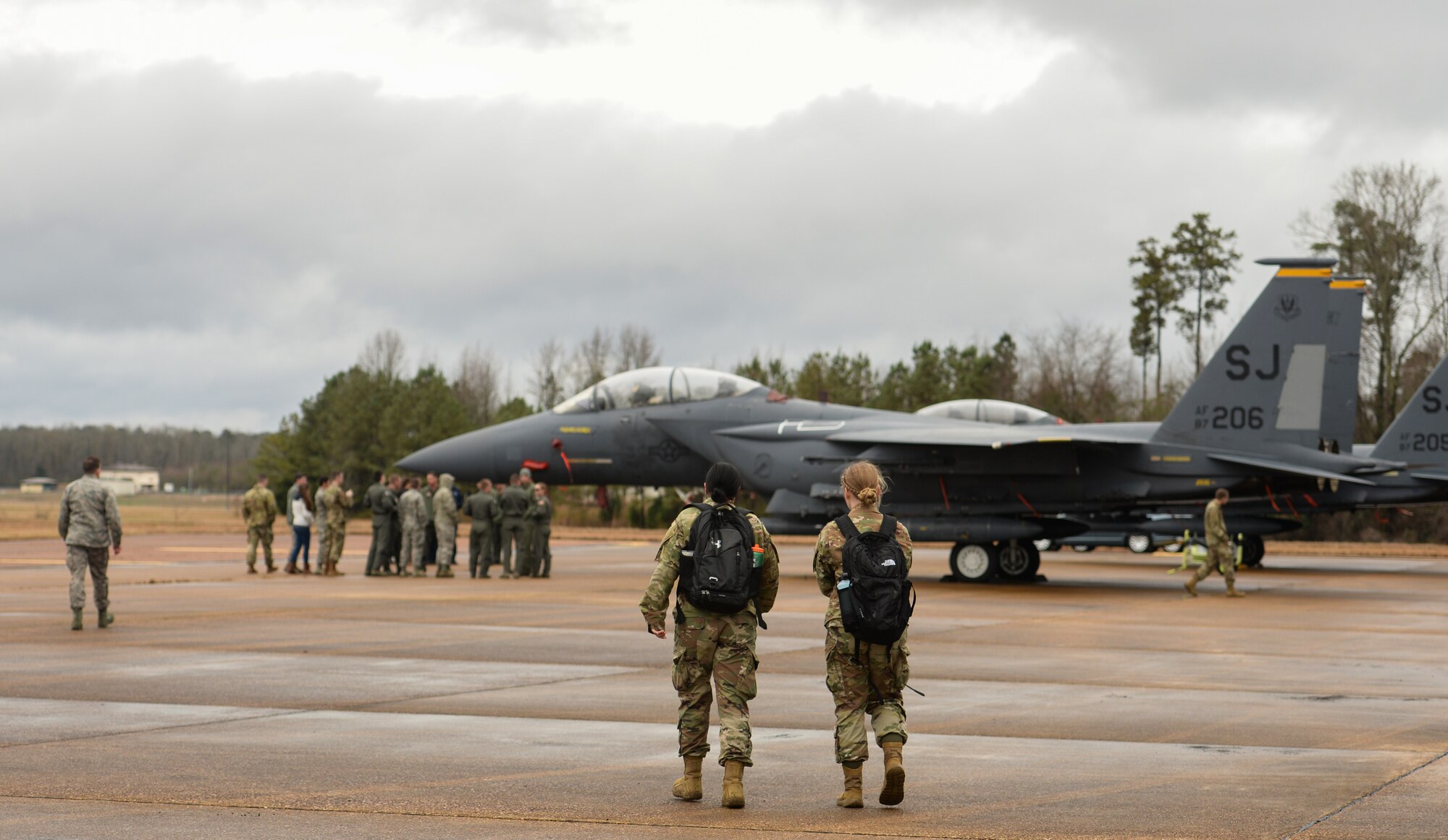 Two Airmen walk toward a group being briefed on the capabilities of the F-15E Strike Eagle Dec. 10, 2019, at Columbus Air Force Base, Miss. An array of avionics and electronics systems gives the F-15E the capability to fight at low altitude, day or night and in all weather. (U.S. Air Force photo by Airman Davis Donaldson)