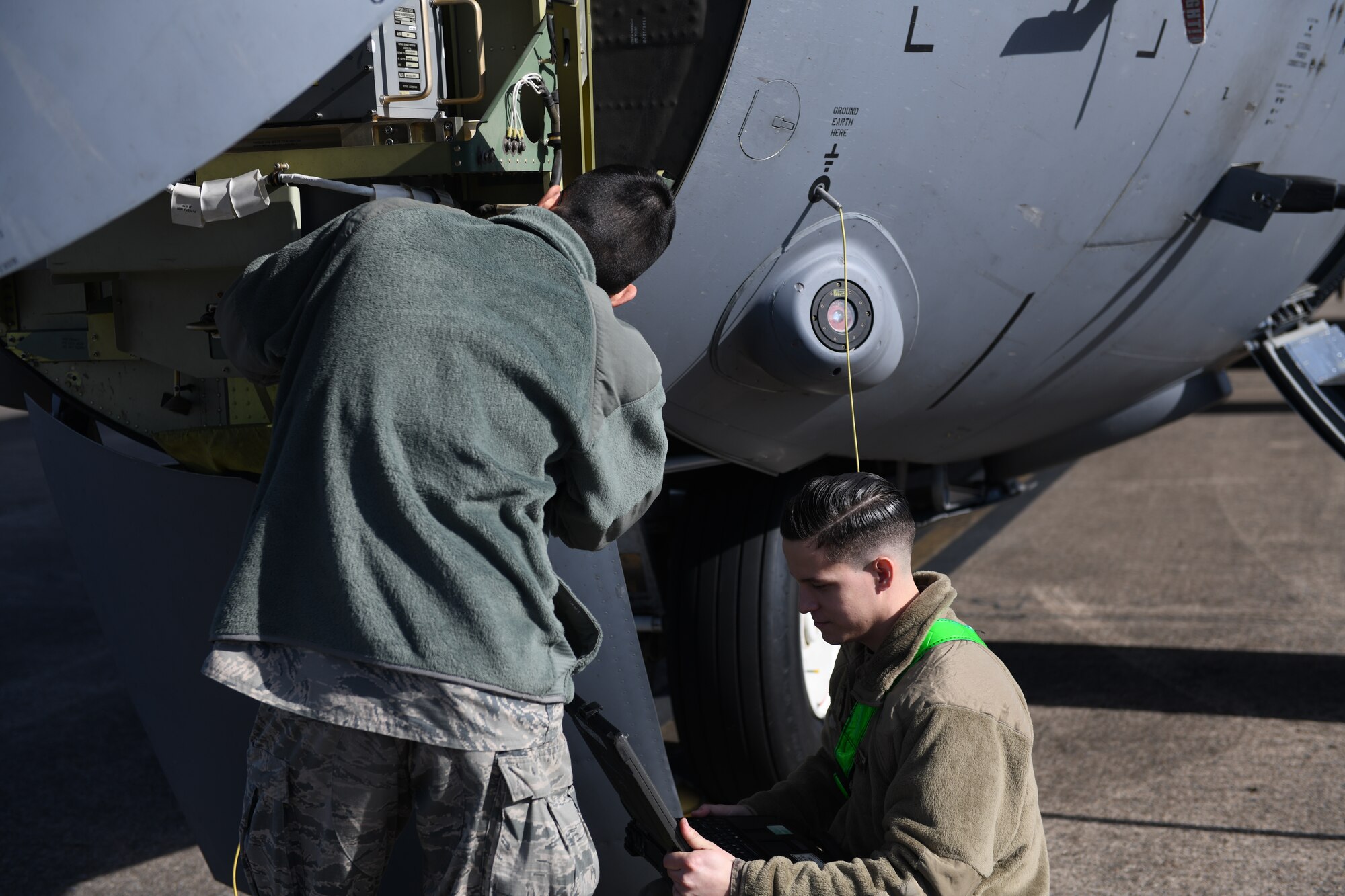 An Airman looks at a computer as another Airman fixes a part of a C-130J Super Hercules.