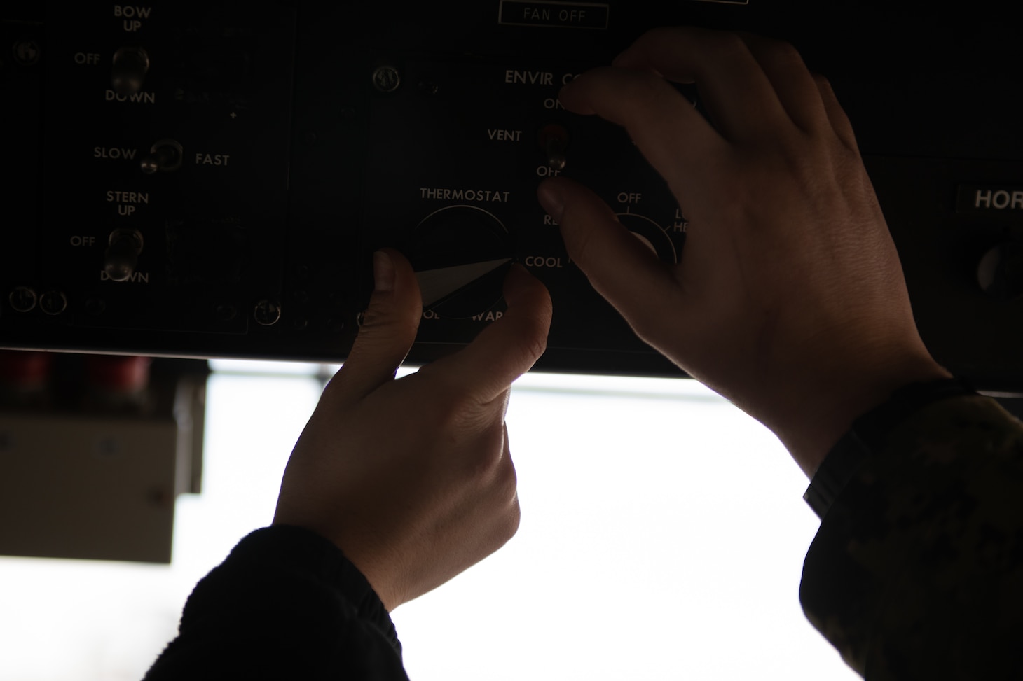 Two hands turning dials on the overhead in the cockpit of an LCAC.