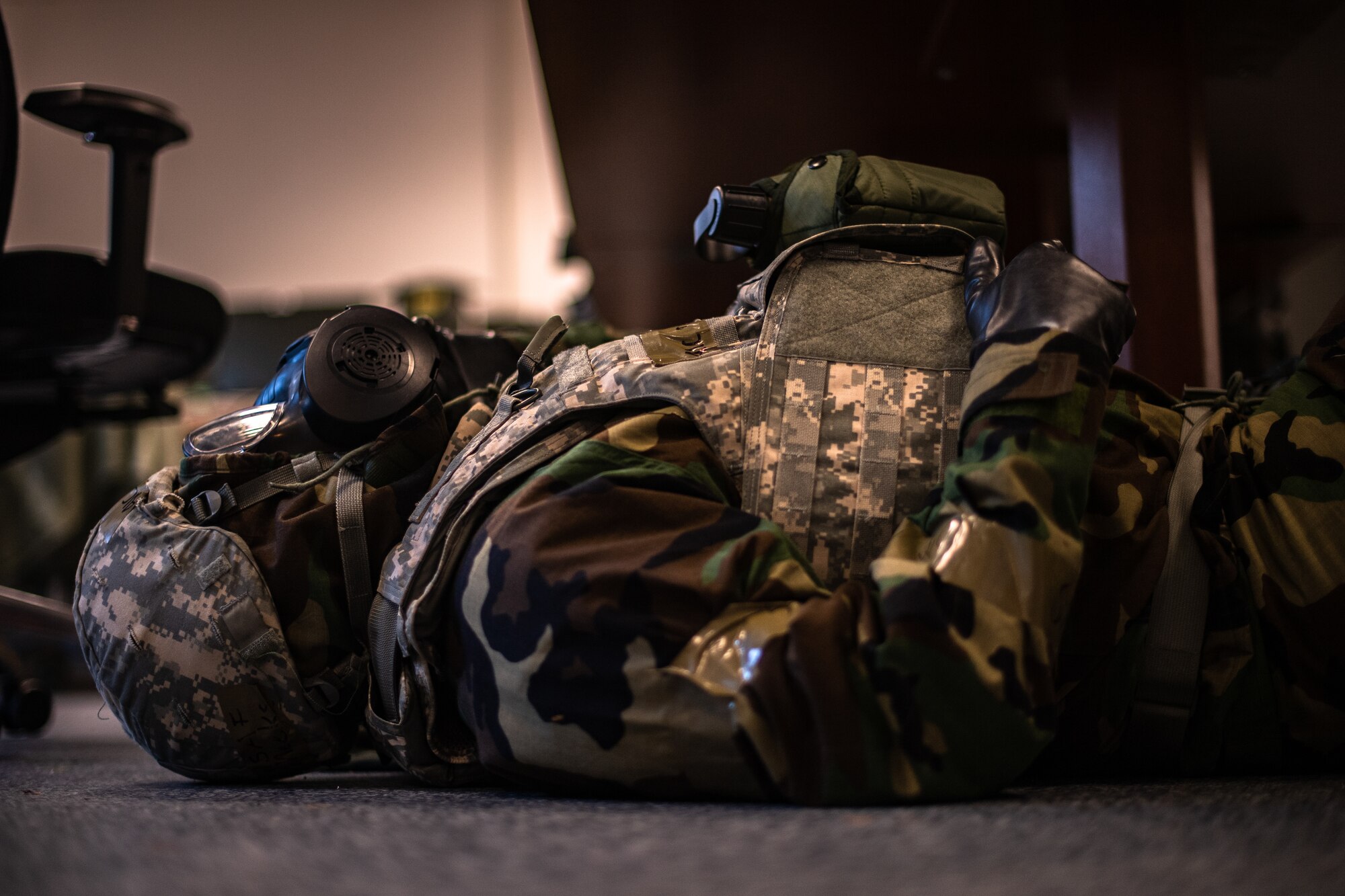 A U.S. Air Force Airman dressed in Mission-Oriented Protective Posture gear takes cover under a desk during exercise Operation Varsity 19-04 at Ramstein Air Base, Germany, Dec. 10, 2019. Airmen had to seek shelter while a simulated air strike occurred over the installation. (U.S. Air Force photo by Staff Sgt. Devin Boyer)
