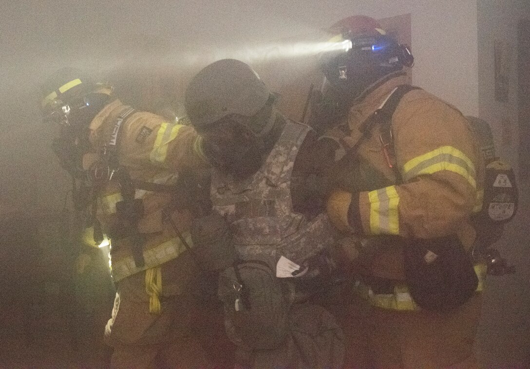 86th Civil Engineer Squadron firefighters help a simulated victim exit a building during an exercise fire scenario at Ramstein Air Base, Germany, Dec. 10, 2019. The scenario began with an aerial attack, resulting in the simulated fire. Exercise participants donned chemical, biological, radiological and nuclear protective training gear as a precaution against simulated chemical weapons.