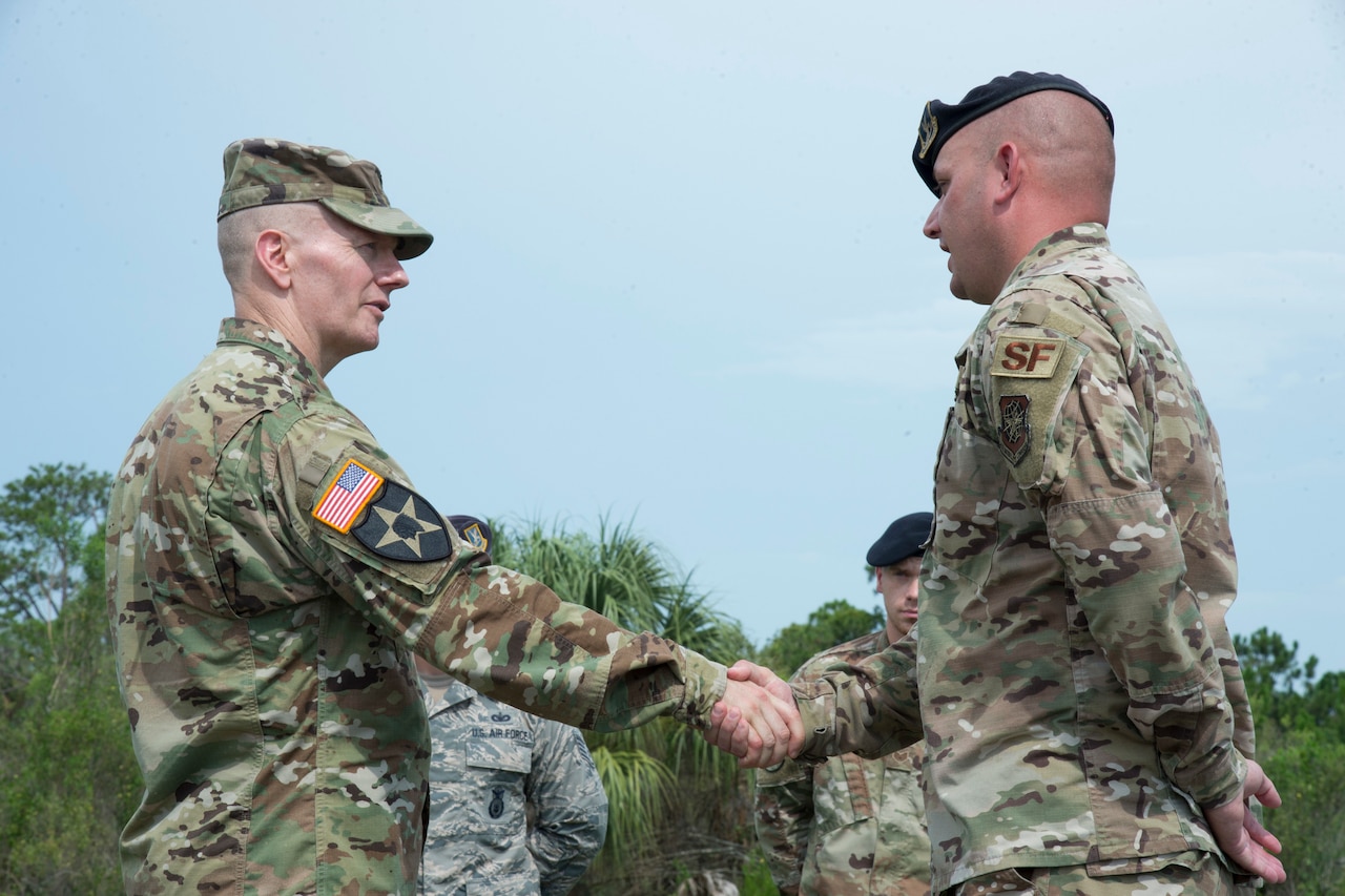 Two men in military uniforms shake hands.