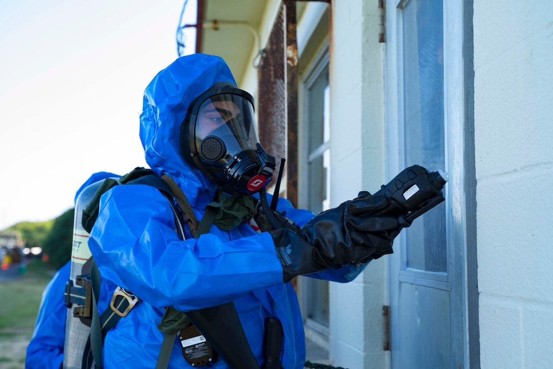 A Marine wears a bio hazard suit while checking a door.
