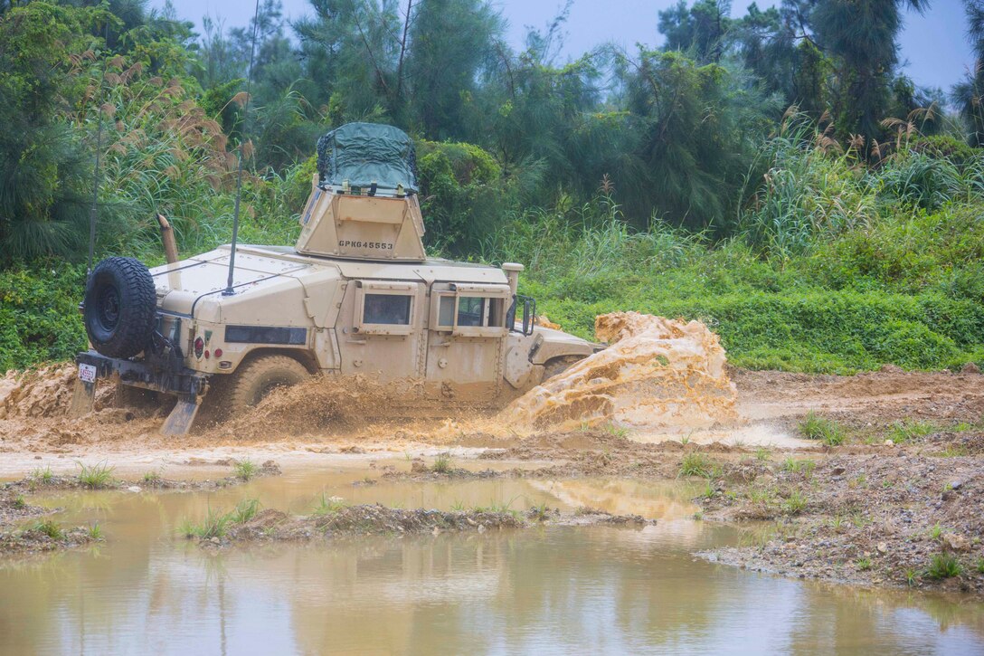 A military vehicle drives through mud and water.