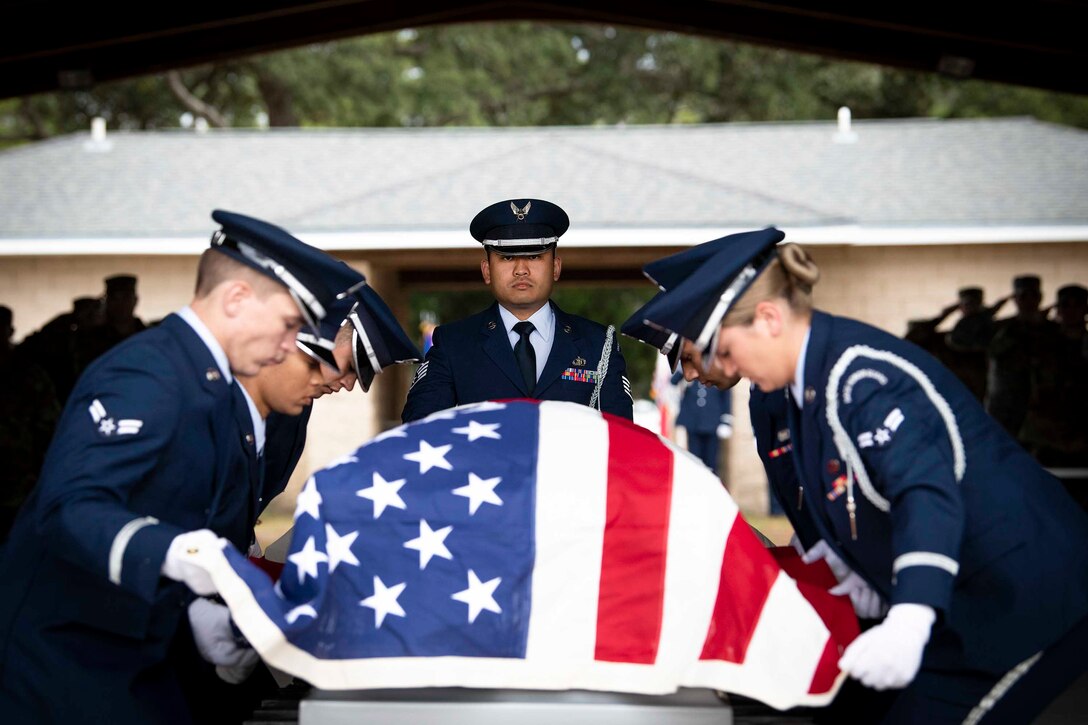 Airmen hold an American flag over a casket.