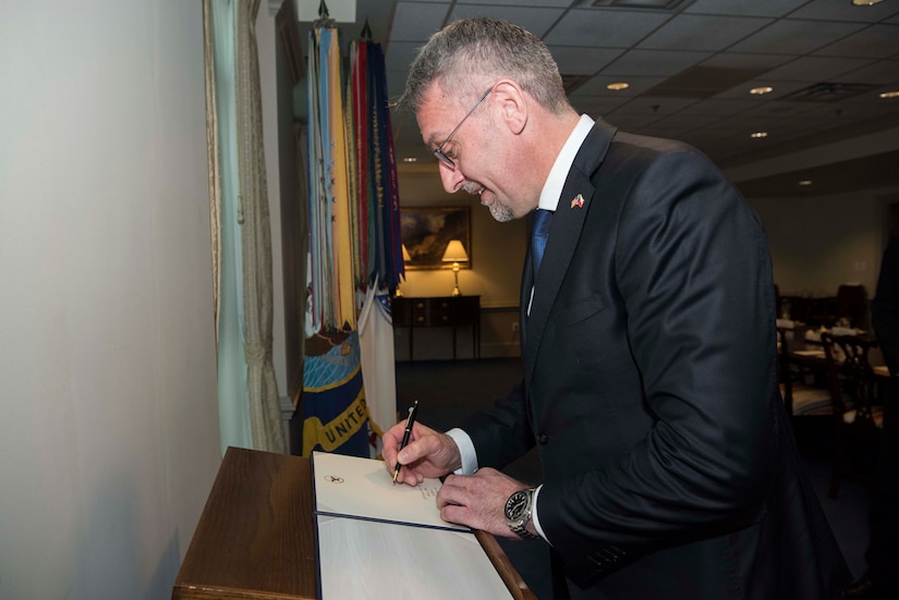 A man writes in a book on a podium.