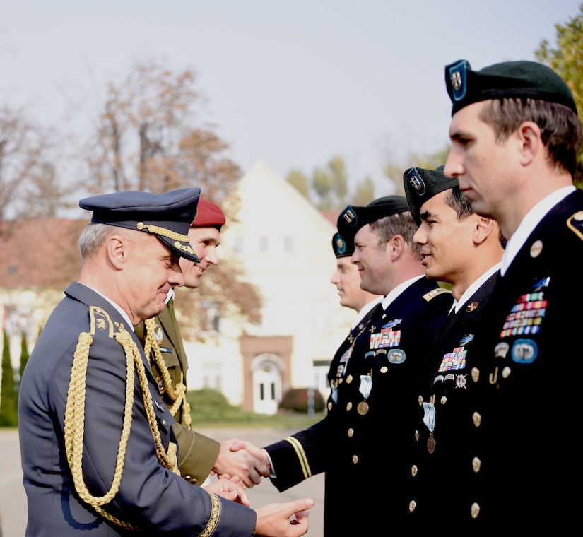 Men in military dress uniforms shake hands.