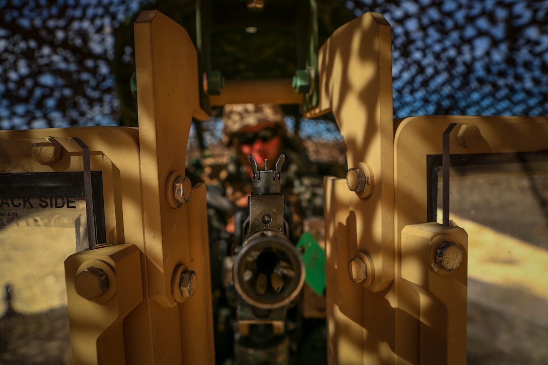 Close view of a machine gun with a Marine manning it in the background.