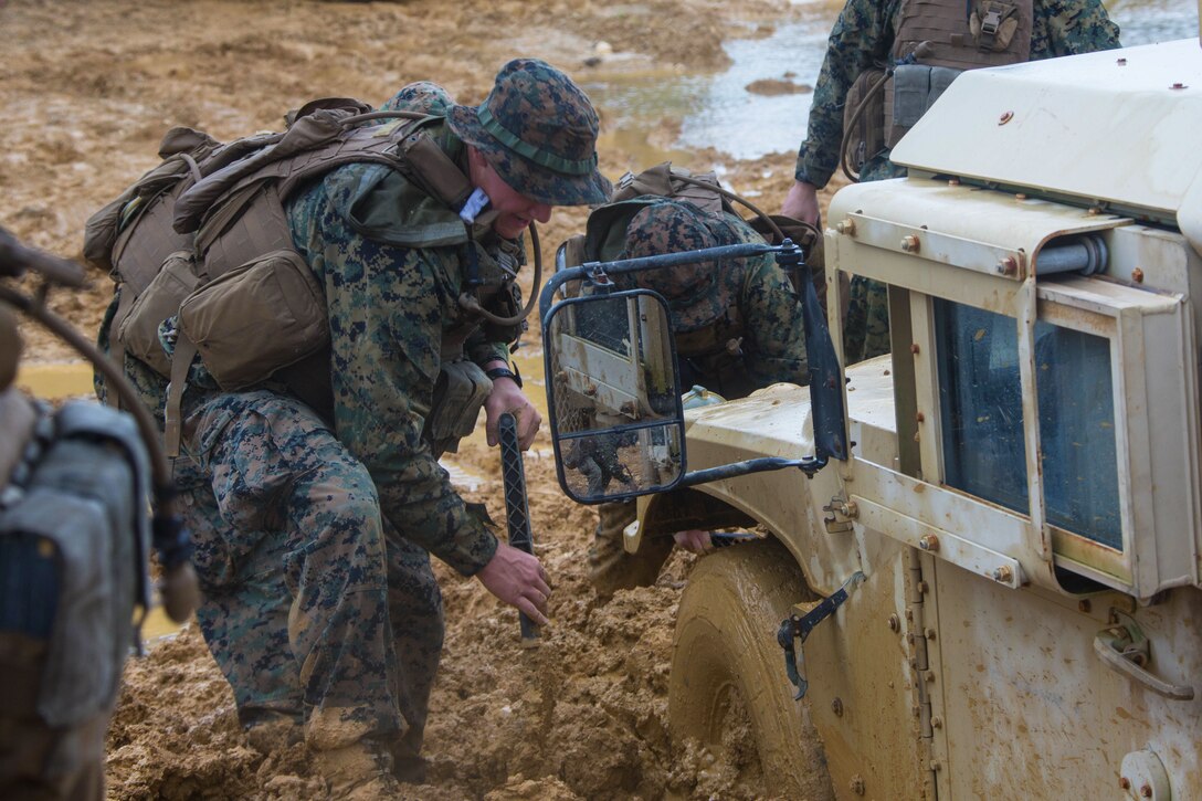 Two Marines dig away mud from a tire on a vehicle.