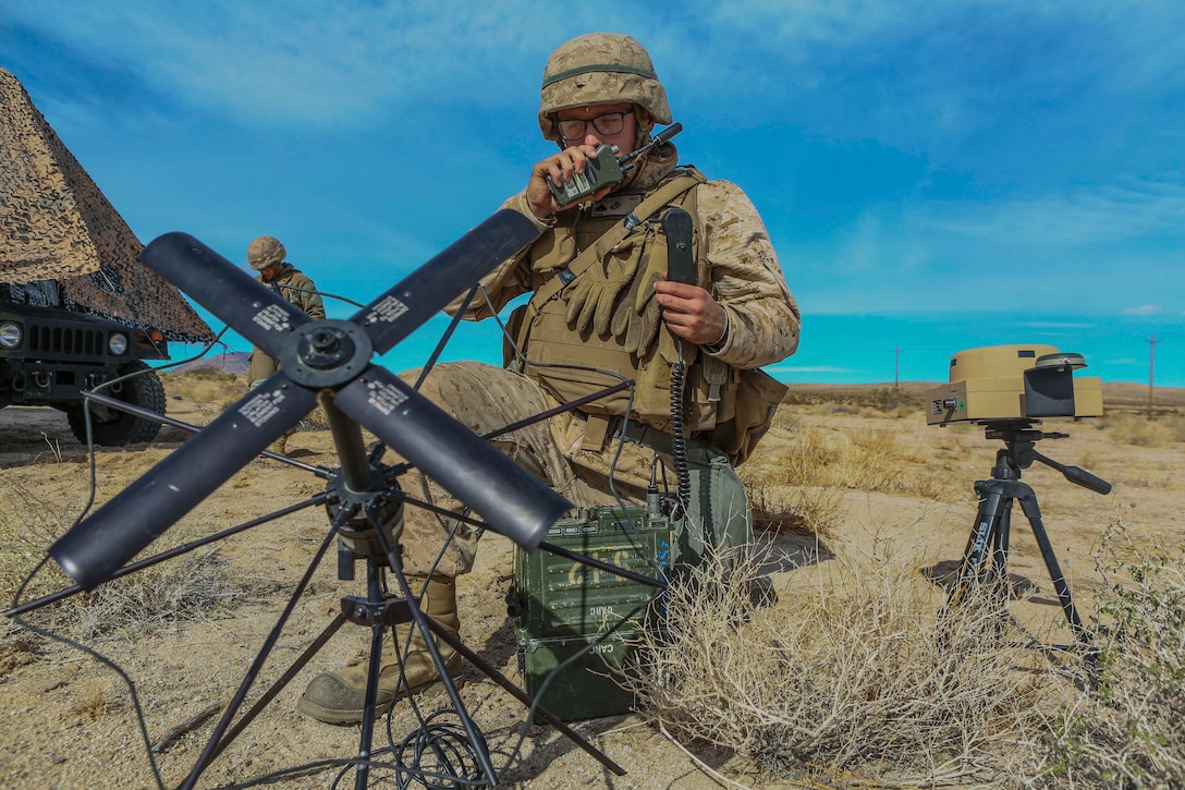 A Marine surrounded by satellite equipment talks on a radio.