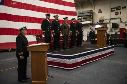 SASEBO, Japan (Dec. 11, 2019) Lt. Cmdr. Kenneth Zilka introduces the official party during the change of command ceremony for Amphibious Squadron (PHIBRON) 11 in the hangar bay of amphibious assault ship USS America (LHA 6). Capt. Richard Lebron relieved Capt. Jim McGovern as commodore of the only forward-deployed amphibious squadron in the U.S. Navy. America, part of Commander, PHIBRON 11 and Expeditionary Strike Group (ESG) 7, is operating in the Indo-Pacific region to enhance interoperability with partners and serve as a ready-response force for any type of contingency.