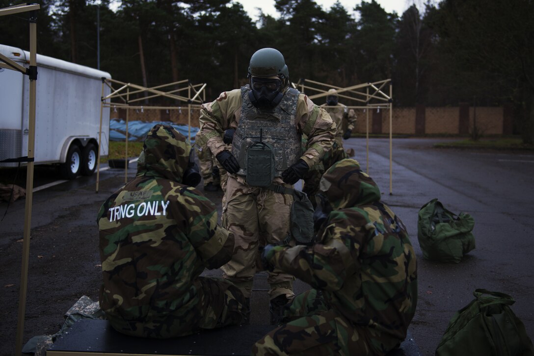 U.S. Air Force Senior Airman Erickson Zinger, 786th Civil Engineer Squadron Emergency Management training journeyman, center, explains to Airmen how to safely remove their Mission-Oriented Protective Posture boot covers at Ramstein Air Base, Germany, Dec 11, 2019. Airmen donned MOPP gear during exercise Operation Varsity 19-04. MOPP gear is used to protect Airmen from chemical, biological, environmental, radiological attacks, which allows mission continuation. (U.S. Air Force Photo by Senior Airman Kaylea Berry)