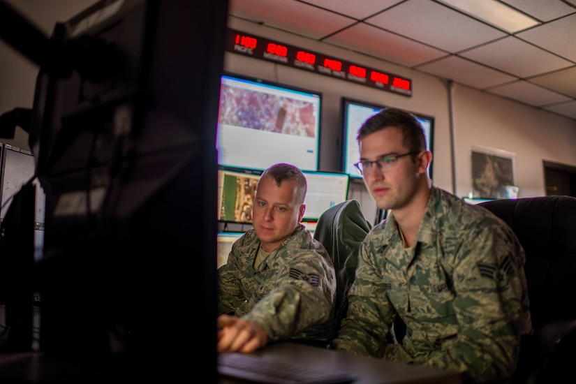 Two airmen focus on a computer screen.