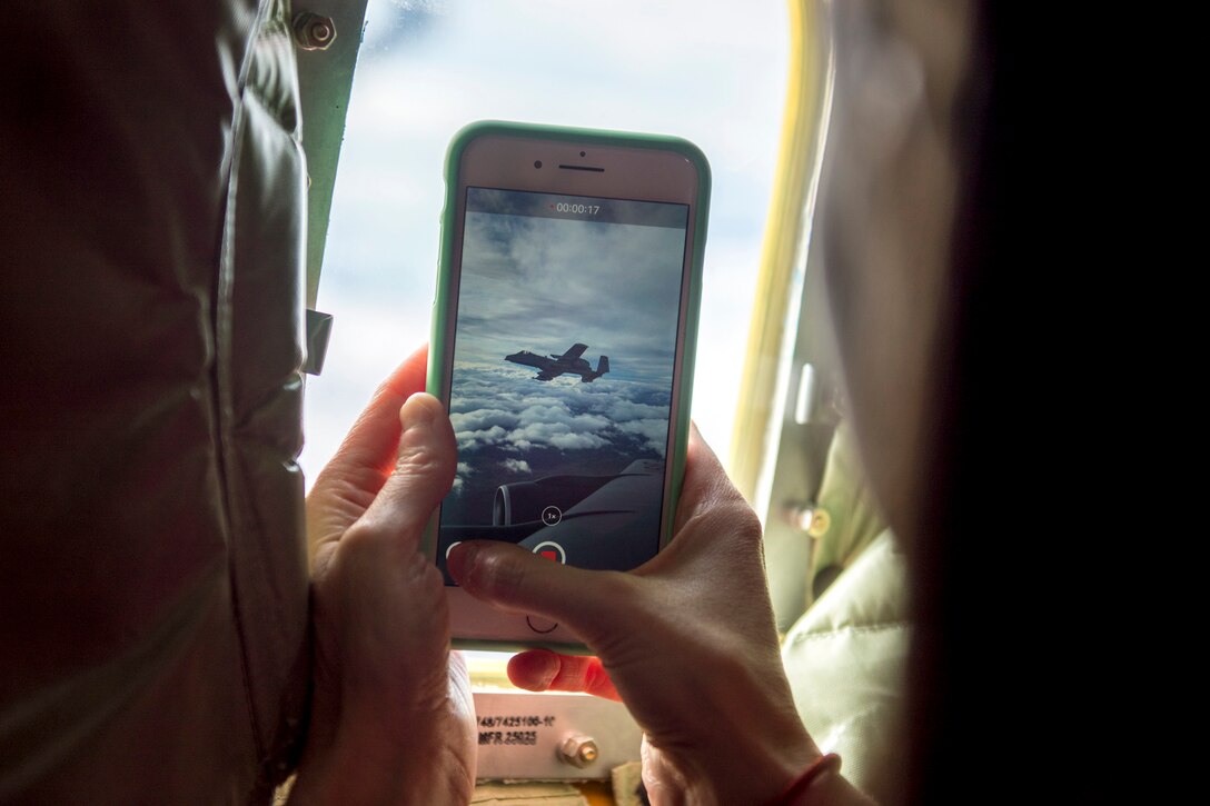 A person uses a smartphone to film an aircraft from the window of another aircraft.