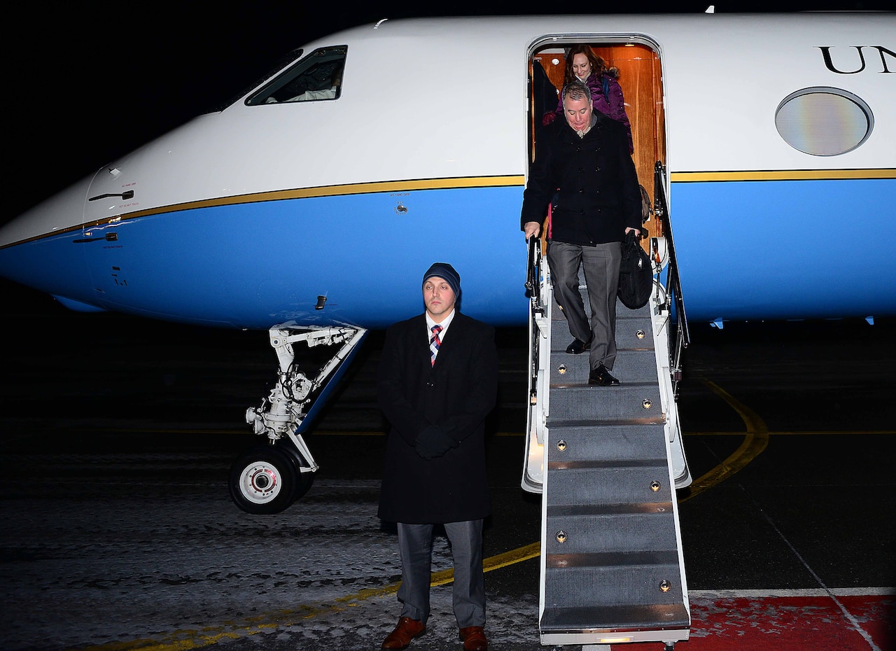 Two people walk down steps off a jet.