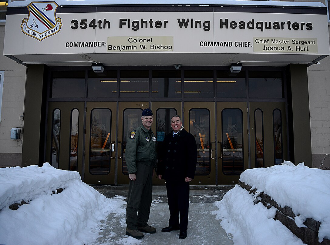 A civilian and an Air Force officer stand in front of a building with snow banks lining the entrance path.