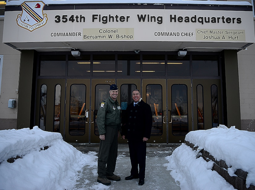A civilian and an Air Force officer stand in front of a building with snow banks lining the entrance path.