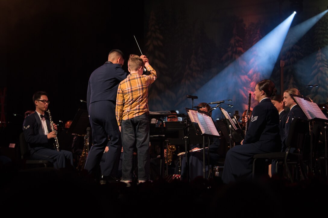 Finnegan Mcdermed, 10, son of U.S. Army Chief Warrant Officer 3, Timothy Mcdermed, general support aviation battalion 5-159, 244th Aviation Brigade, conducts the U.S. Air Force Heritage of America band as they perform at a holiday concert at the Christopher Newport University Ferguson Center, Newport News, Virginia, Dec. 5, 2019. Finnegan was selected to conduct the band after his mother posted a photo of him at the concert on social media. (U.S. Air Force photo by Airman 1st Class Sarah Dowe)