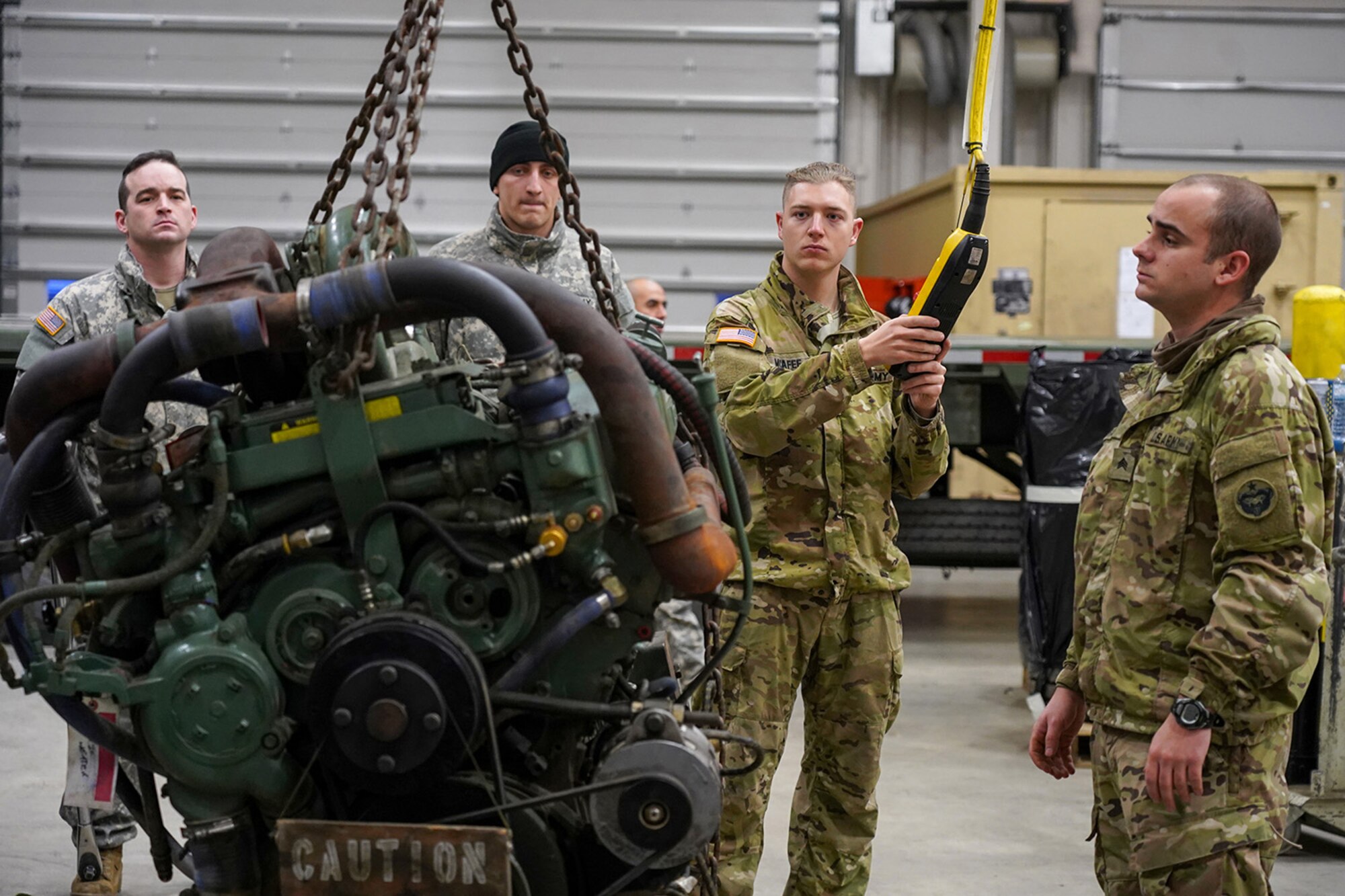 Army Spc. Bradley McAfee, a native of Reading, Penn., center, assigned to the 109th Transportation Company, 17th Combat Sustainment Support Battalion, U.S. Army Alaska, controls a hoist while moving a damaged engine from an M984A2 Heavy Expanded Mobility Tactical Truck wrecker his unit’s motor pool on Joint Base Elmendorf-Richardson, Alaska, Dec. 13, 2019. The M984A2 is an eight-wheel drive, diesel-powered, variant of the HEMTT used in vehicle recovery operations.
