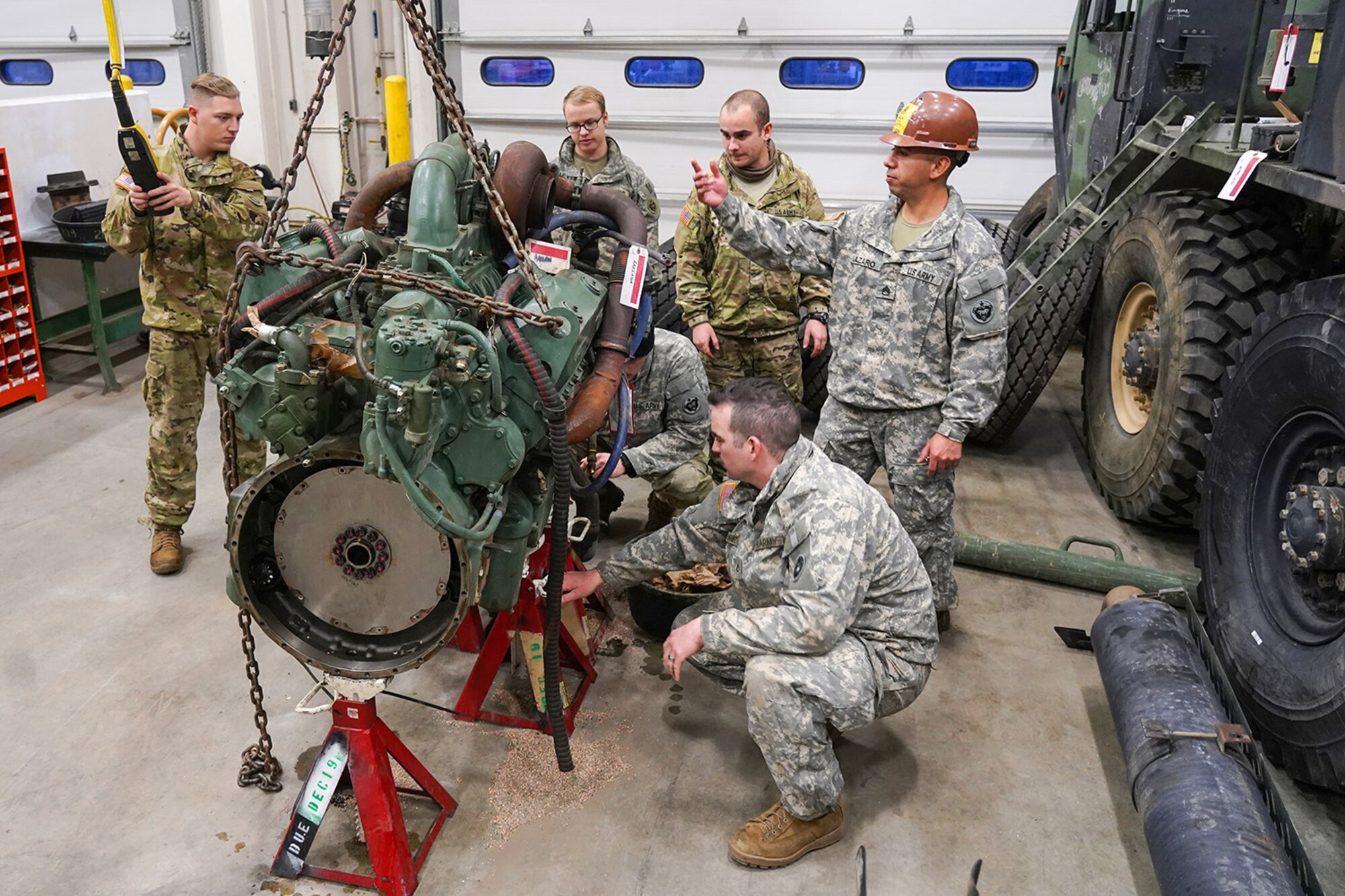 Army Staff Sgt. Federico Lazaro, a native of Chicago, right, assigned to the 109th Transportation Company, 17th Combat Sustainment Support Battalion, U.S. Army Alaska, supervises his Soldiers moving a damaged engine from an M984A2 Heavy Expanded Mobility Tactical Truck wrecker with a hoist in their motor pool on Joint Base Elmendorf-Richardson, Alaska, Dec. 13, 2019. The M984A2 is an eight-wheel drive, diesel-powered, variant of the HEMTT used in vehicle recovery operations.