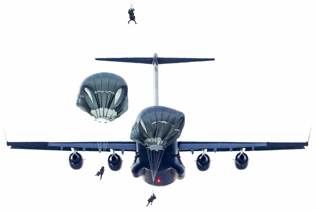 Soldiers jump out of a plane as the plane flies behind.