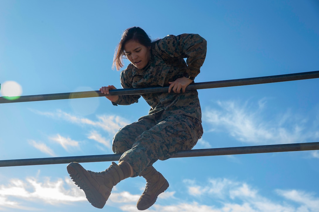 A Marine climbs over metal bars.