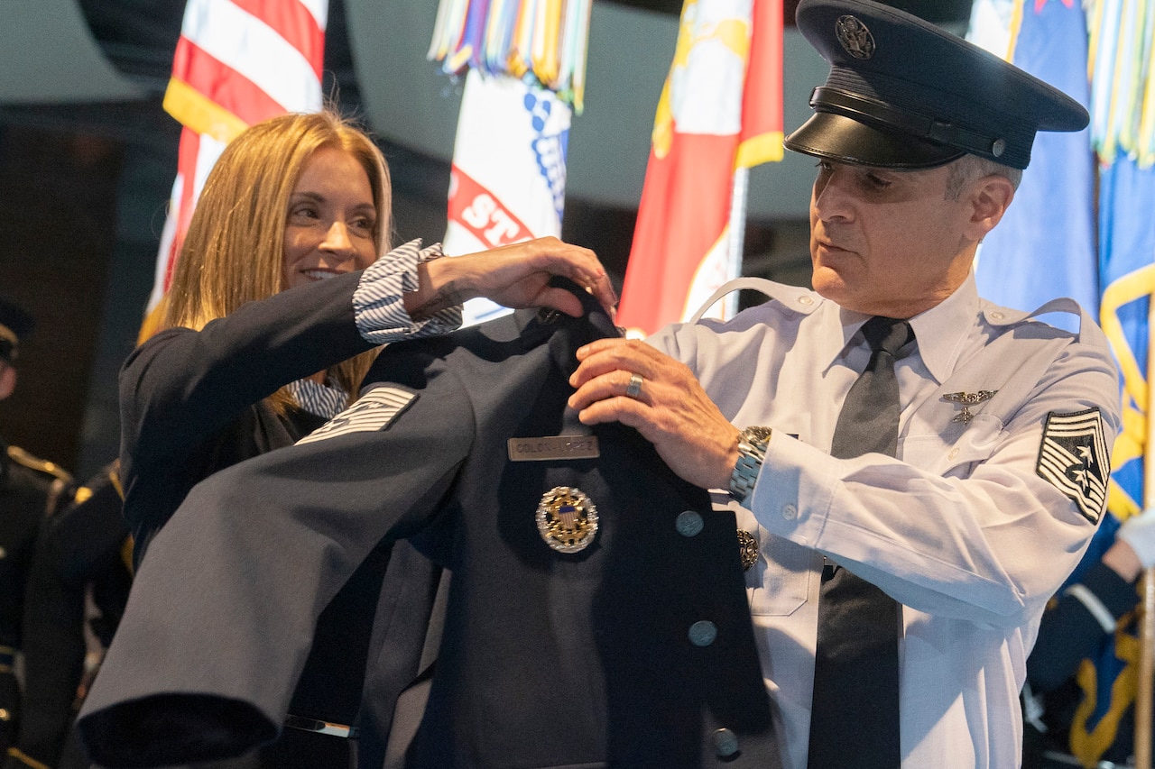 The wife of Senior Enlisted Advisor to the Chairman of the Joint Chiefs of Staff Ramon "CZ" Colon-Lopez hands him a jacket.