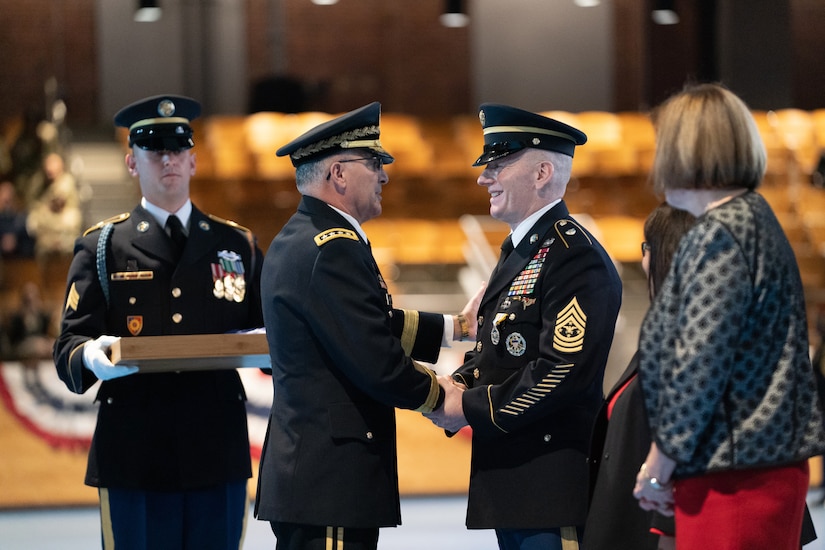 Two service members shake hands as others look on.