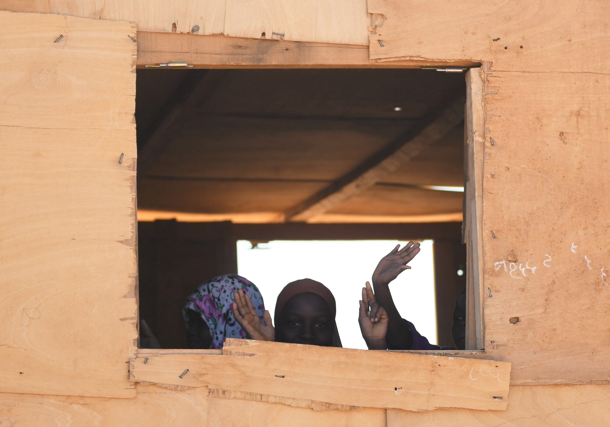 School children wave from inside an older classroom in the village of Tadress, Niger, Dec. 12, 2019. Coordinated by members of the U.S. Army 443rd Civil Affairs Battalion CAT 219, Airmen deployed to the 724th Expeditionary Air Base Squadron Civil Engineer Flight, Nigerien Air Base 201, constructed a new classroom for the students. In Niger, a teacher is only assigned to a class if there is a building to teach in. (U.S. Air Force photo by Staff Sgt. Alex Fox Echols III)