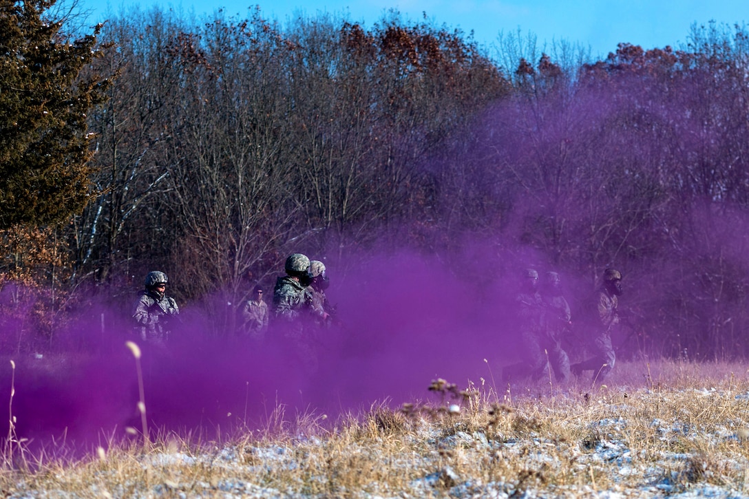 Soldiers move through purple smoke in a field.