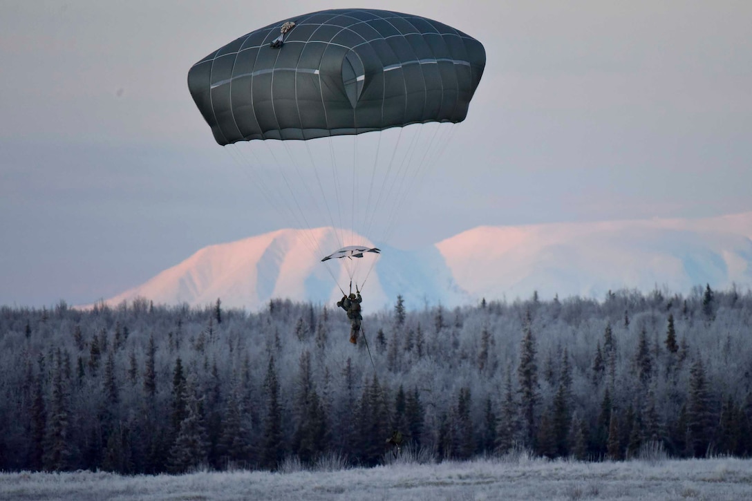 A soldier descends through the sky while wearing a parachute.