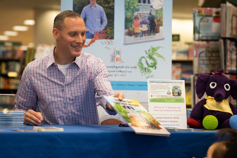 Marine Maj. Joseph Goodrich hands a children’s book to a young reader at a book store in Jacksonville, North Carolina, Nov. 30, 2019. Goodrich, now a published author, read his book to fans and signed copies of his book for young readers. Goodrich is the executive officer of Marine Aerial Refueler Transport Squadron 252. (U.S. Marine Corps photo by Cpl. Cody Rowe)