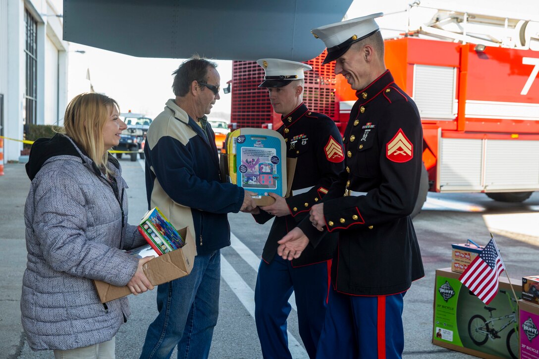 Two Marines accept toys from two civilians outside an airport.