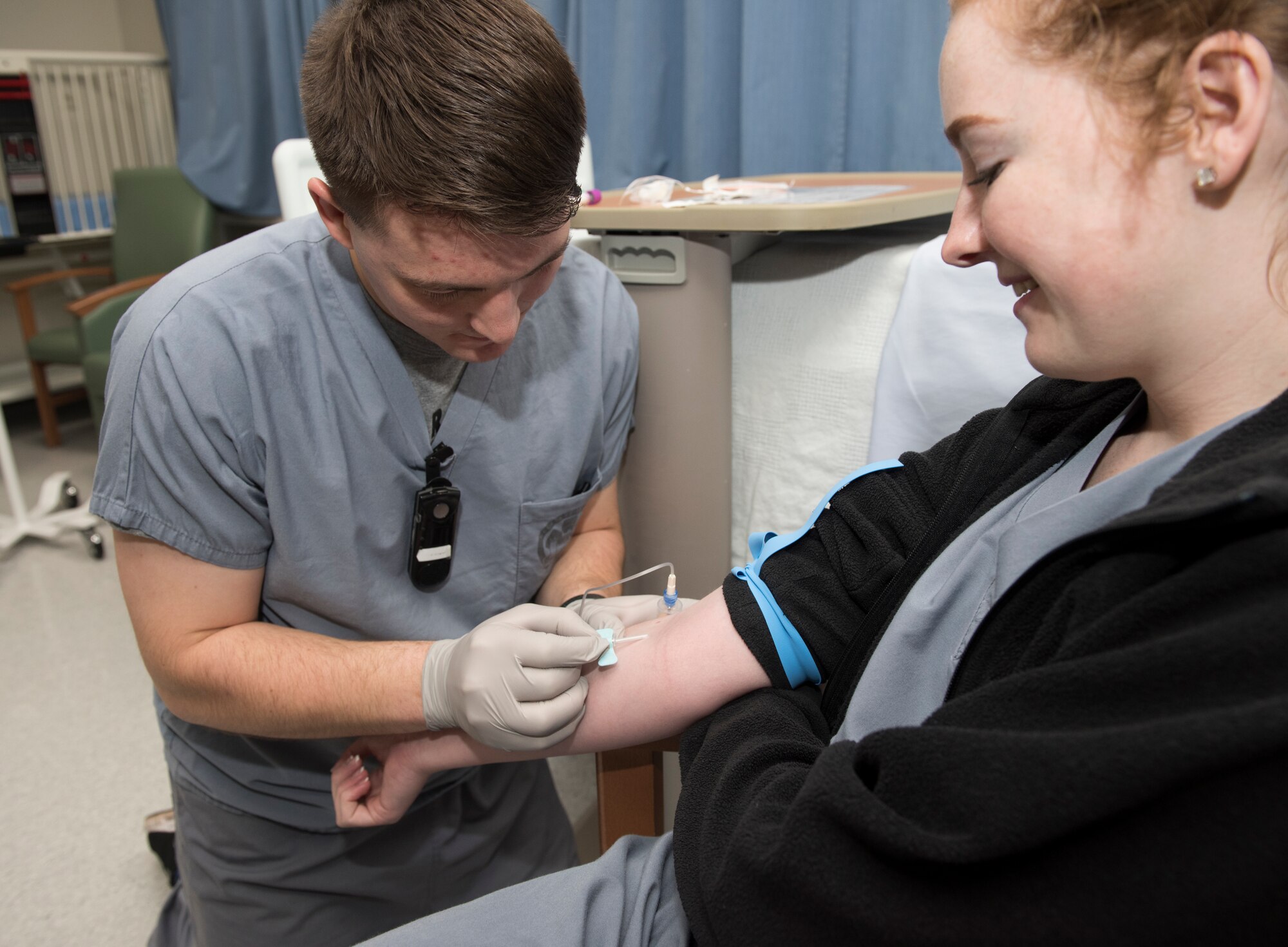 U.S. Air Force Airman 1st Class Nicolas Bertuna, left, 86th Medical Squadron aerospace medical technician demonstrates to U.S. Air Force Airman 1st Class Hayley Bell, 86th MDS medic, how to draw blood at Landstuhl Regional Medical Center, Dec. 13, 2019. The 86th Airlift Wing named Bertuna Airlifter of the Week for his accomplishments, including being the only Airman at LRMC to lead U.S. Army physical training three times a week.