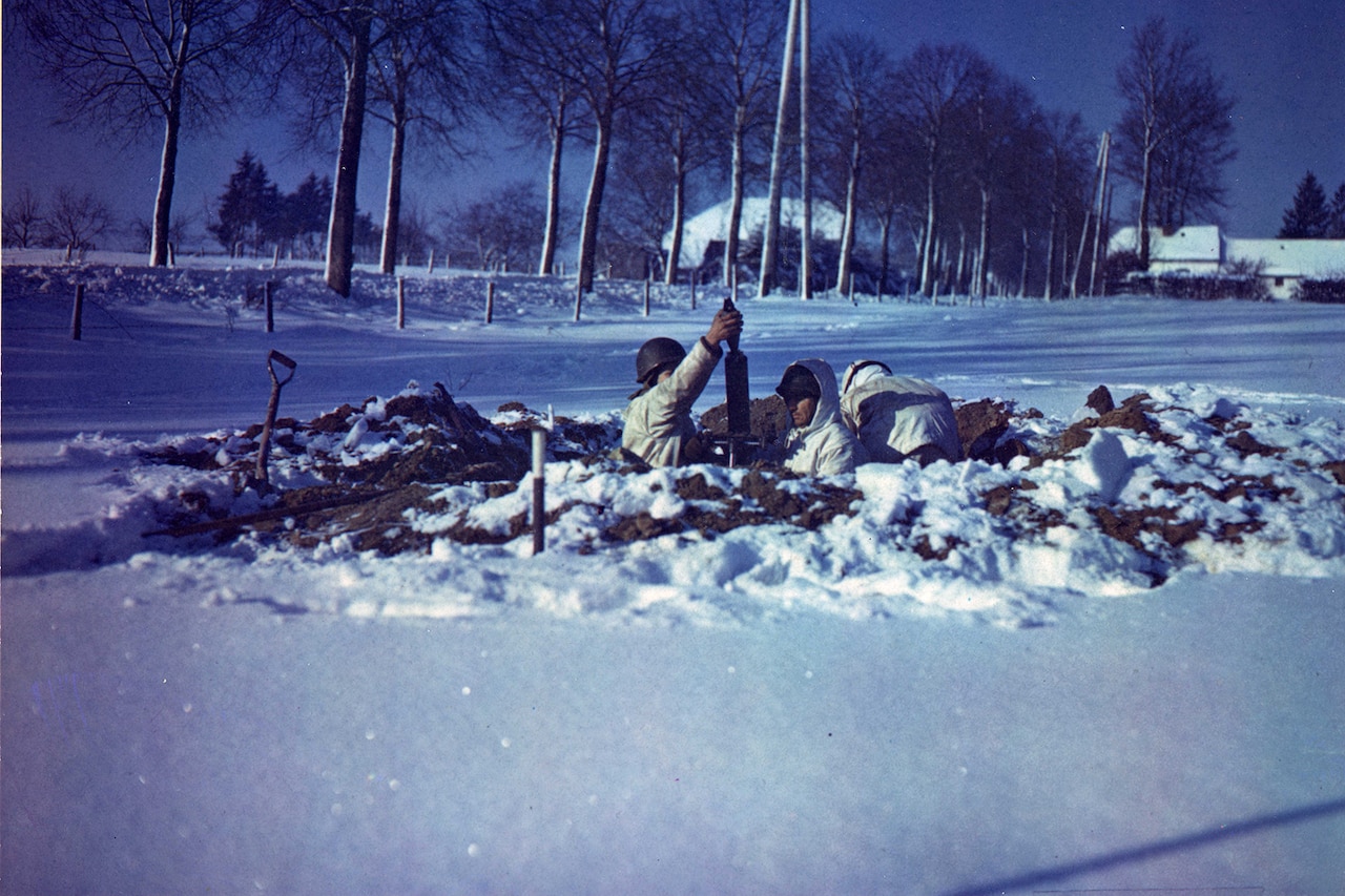 Soldiers operate weapons inside a hole that’s been dug into the snow-covered ground.