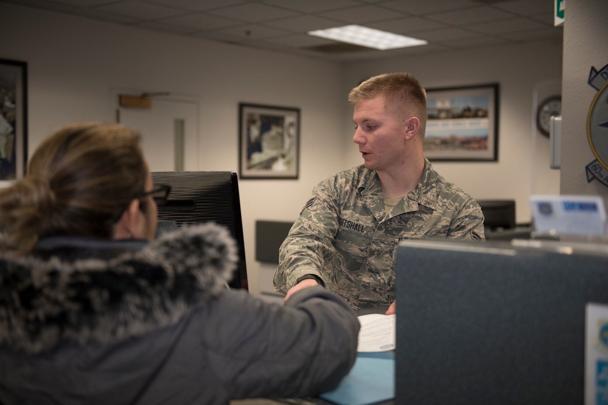 U.S. Air Force Airman 1st Class Elijah Cutshall, 60th Aerial Port Squadron air transportation agent, hands Rochelle Hathway, military spouse, itinerary information for her flight Dec. 6, 2019, at Travis Air Force Base, California. Cutshall greeted customers at the front desk to answer any questions they had. (U.S. Air Force photo by Airman 1st Class Cameron Otte)