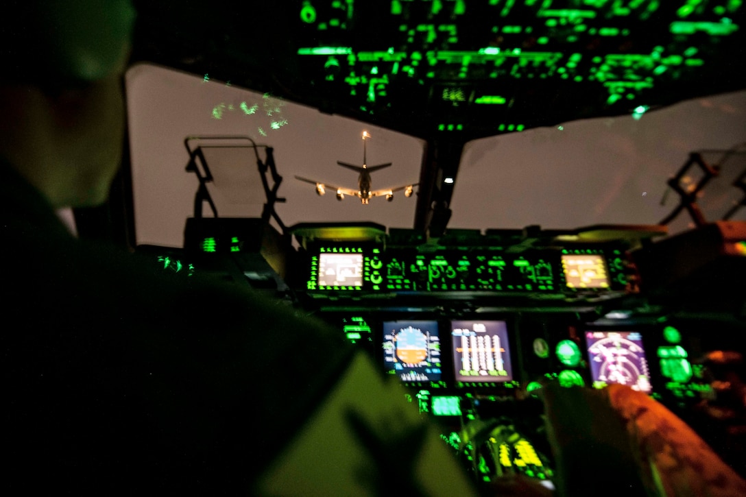 A pilot sits in a cockpit with green lights.