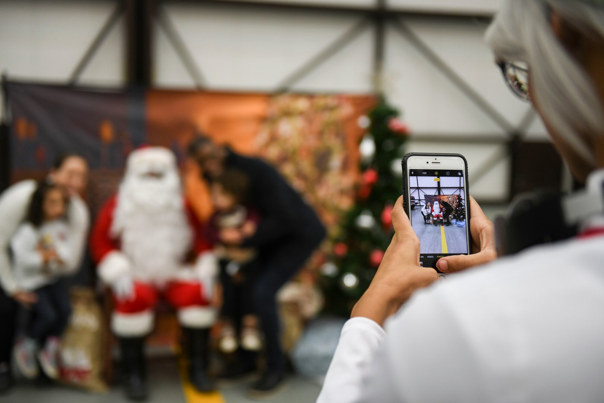 A volunteer dressed as Santa’s helper takes a photo of a family posing with Santa Claus at the children’s holiday party at RAF Mildenhall, England, Dec. 14, 2019.  The children’s holiday party was hosted by the Mildenhall Spouses’ Association in partnership with the 100th Force Support Squadron to provide various holiday-themed activities for Team Mildenhall children and families. (U.S. Air Force photo by Staff Sgt. Lexie West)