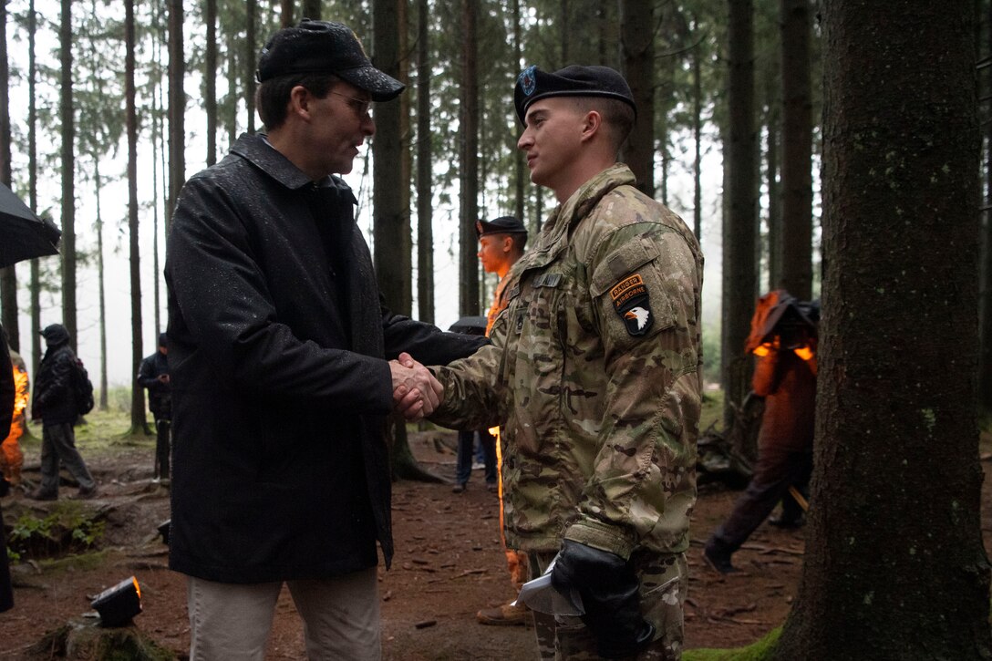 Defense Secretary Dr. Mark T. Esper shakes hands with a member of the 101st Airborne Division in a wooded area.