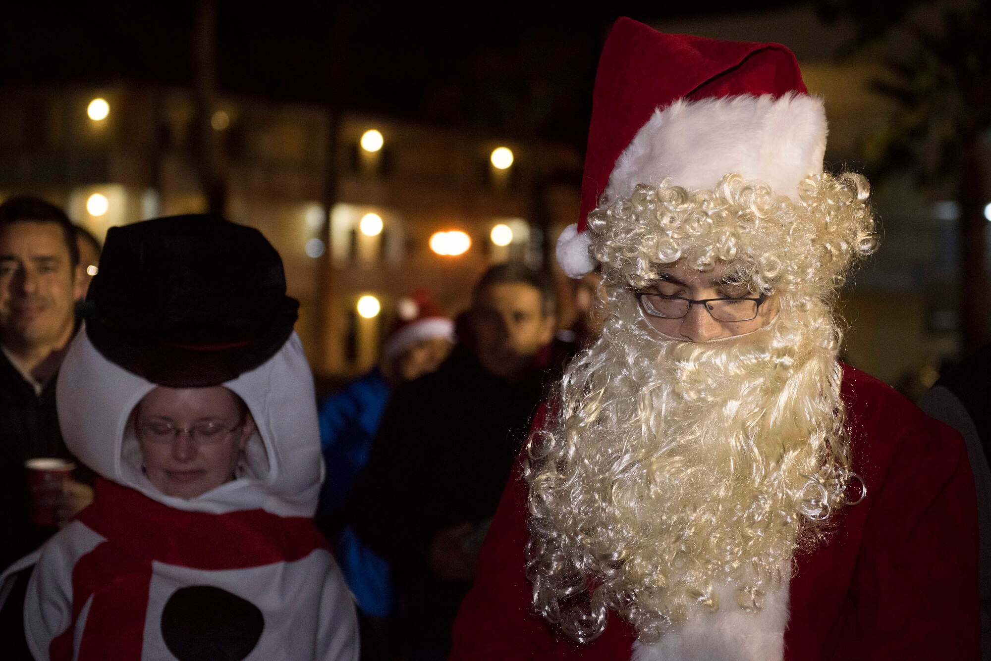 Participants dressed in holiday costumes bow their heads for an invocation during the base tree lighting ceremony Dec. 5, 2019, at Incirlik Air Base, Turkey. U.S. military members stationed overseas share aspects of American culture in the countries they visit. (U.S. Air Force photo by Staff Sgt. Joshua Magbanua)